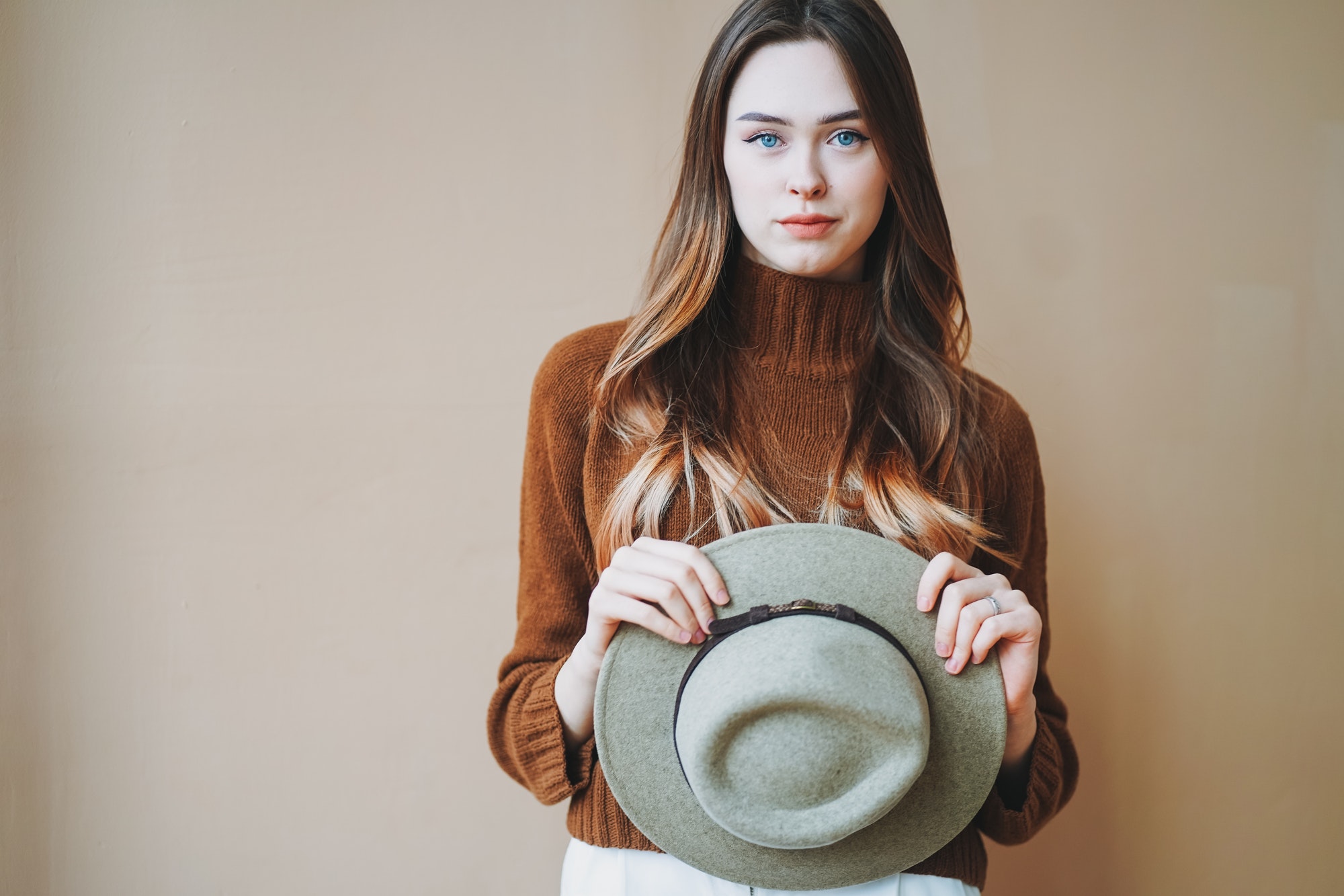 Young beautiful long brown-haired hair girl with blue eyes in felt hat and brown knitted sweater