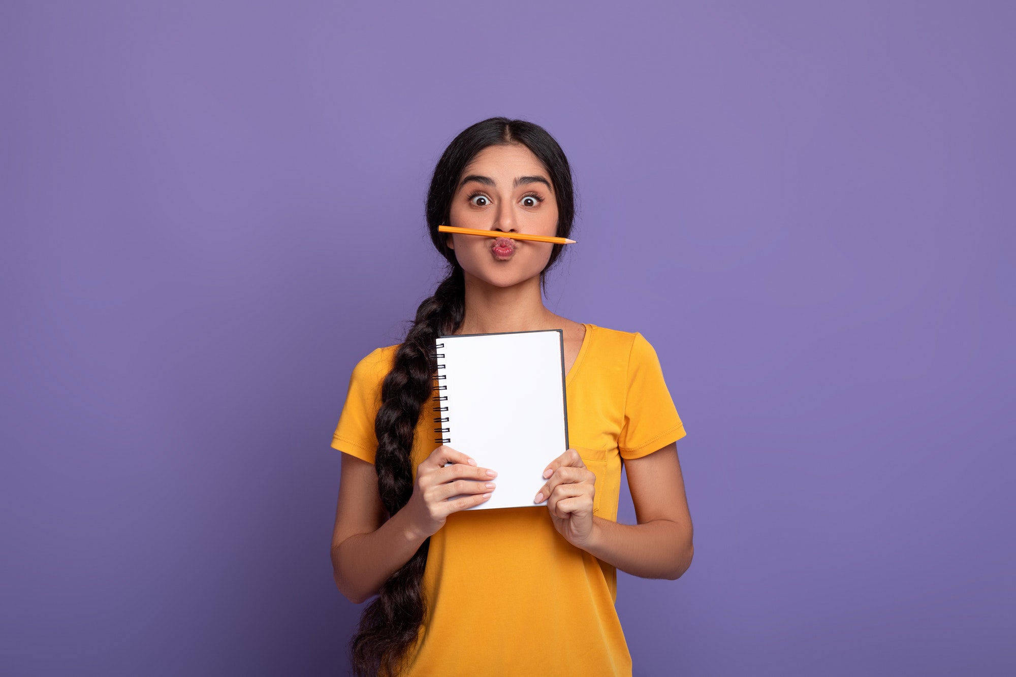 Funny indian lady holding pen as moustache over purple wall