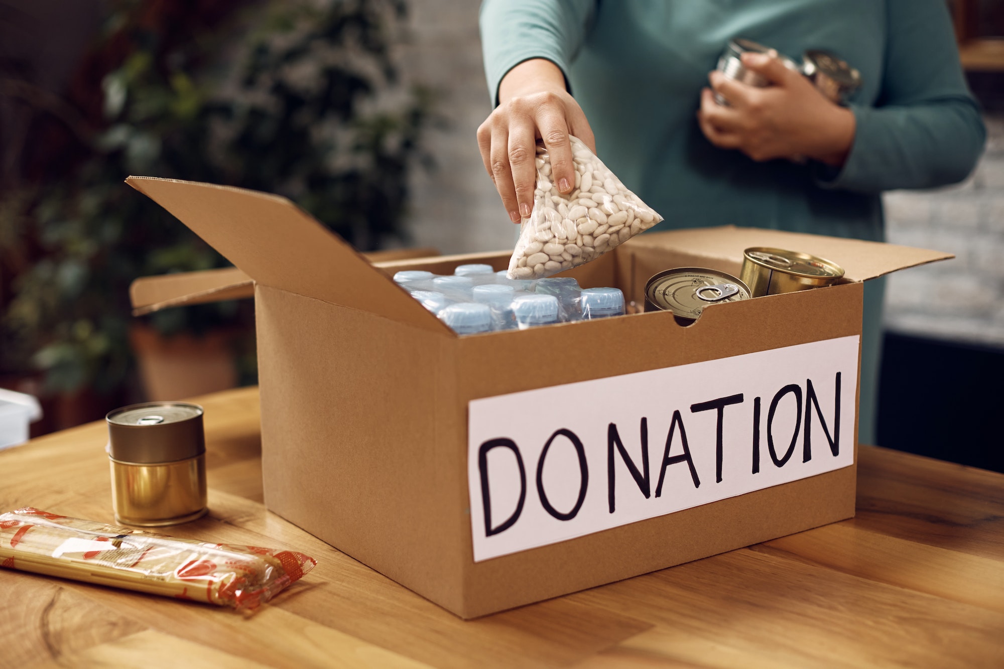 Close-up of volunteer packing food in donation box for charity food bank.