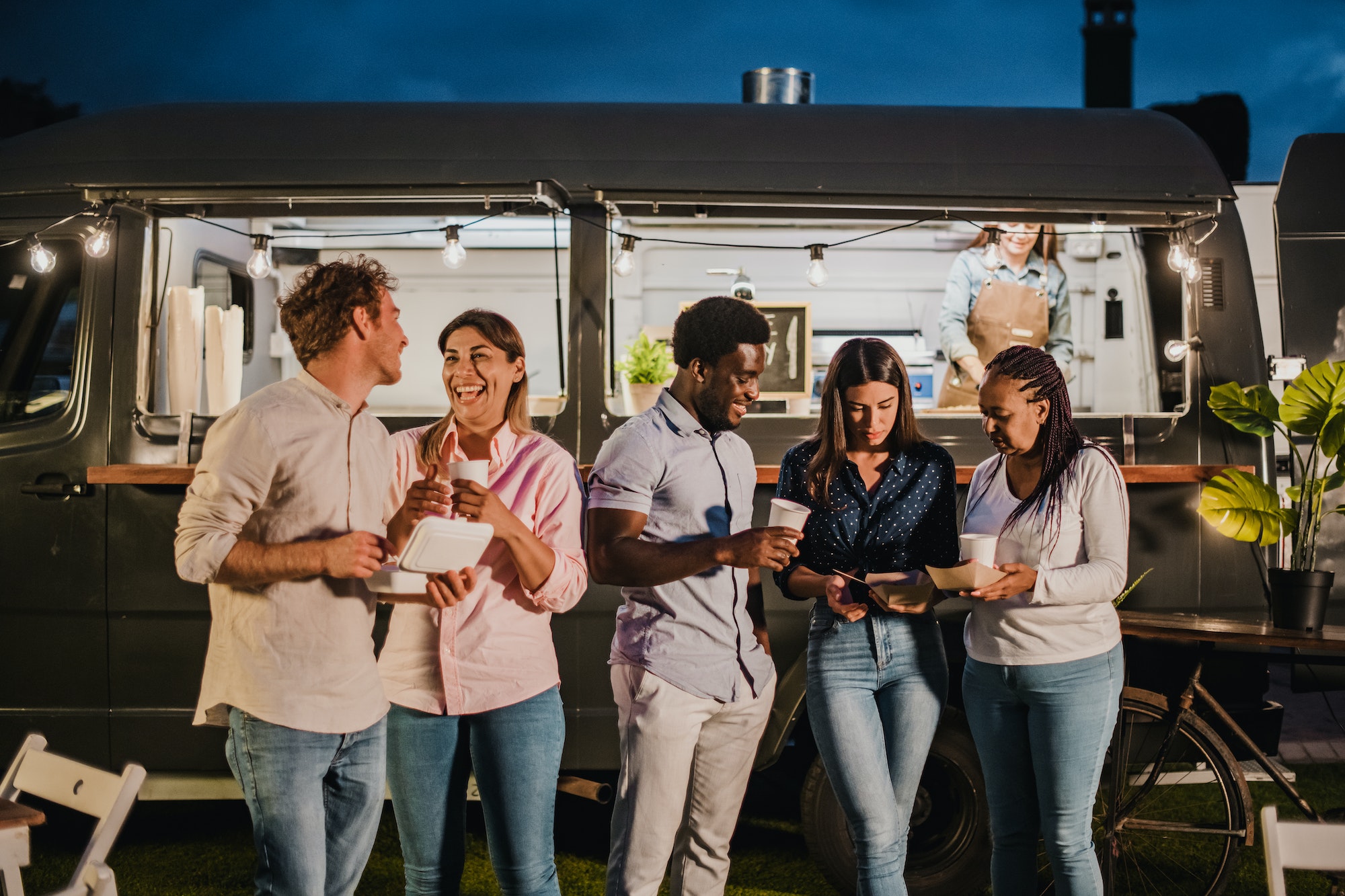 Multiethnic friends resting outside food truck in evening