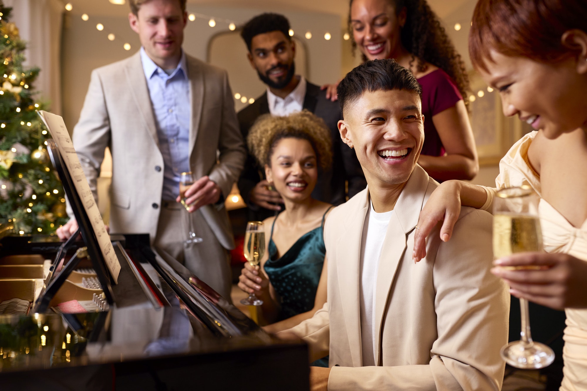 Group Of Friends Around Piano Celebrating At Christmas Or New Year Party Together