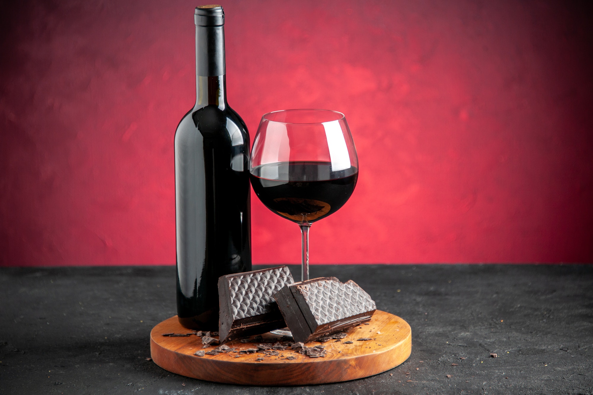 front view wine glass pieces of dark chocolate black wine bottle on wood board on dark red front view wine glass pieces of dark chocolate black wine bottle on wood board on dark red