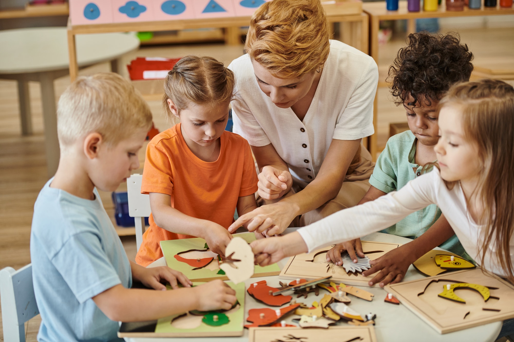 teacher playing with interracial children with didactic materials in montessori school