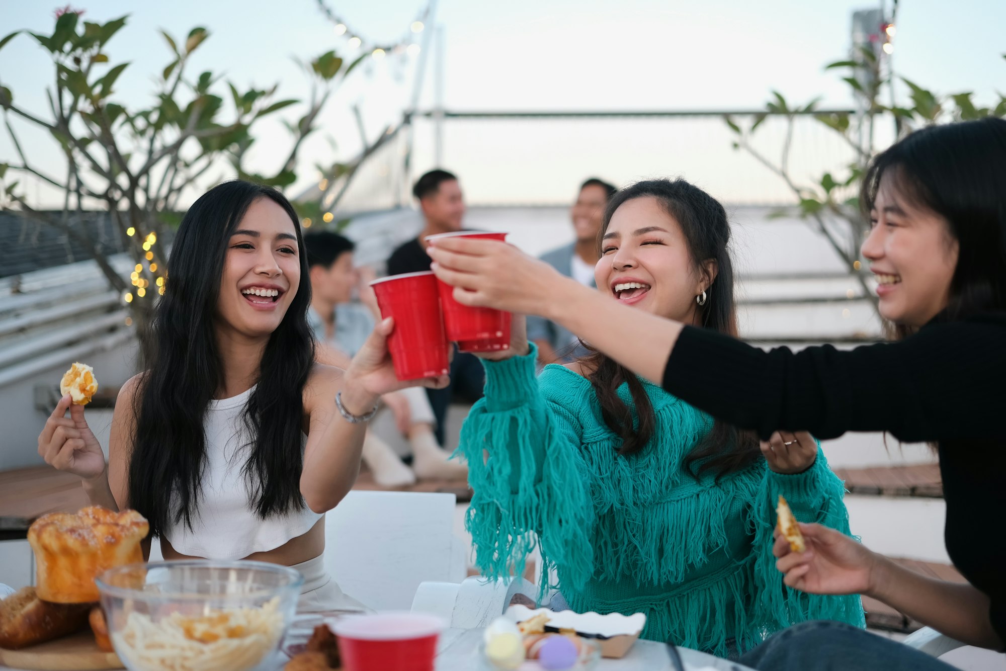 Cheerful male and female friends enjoying happy hour at terrace party and toasting drinks.