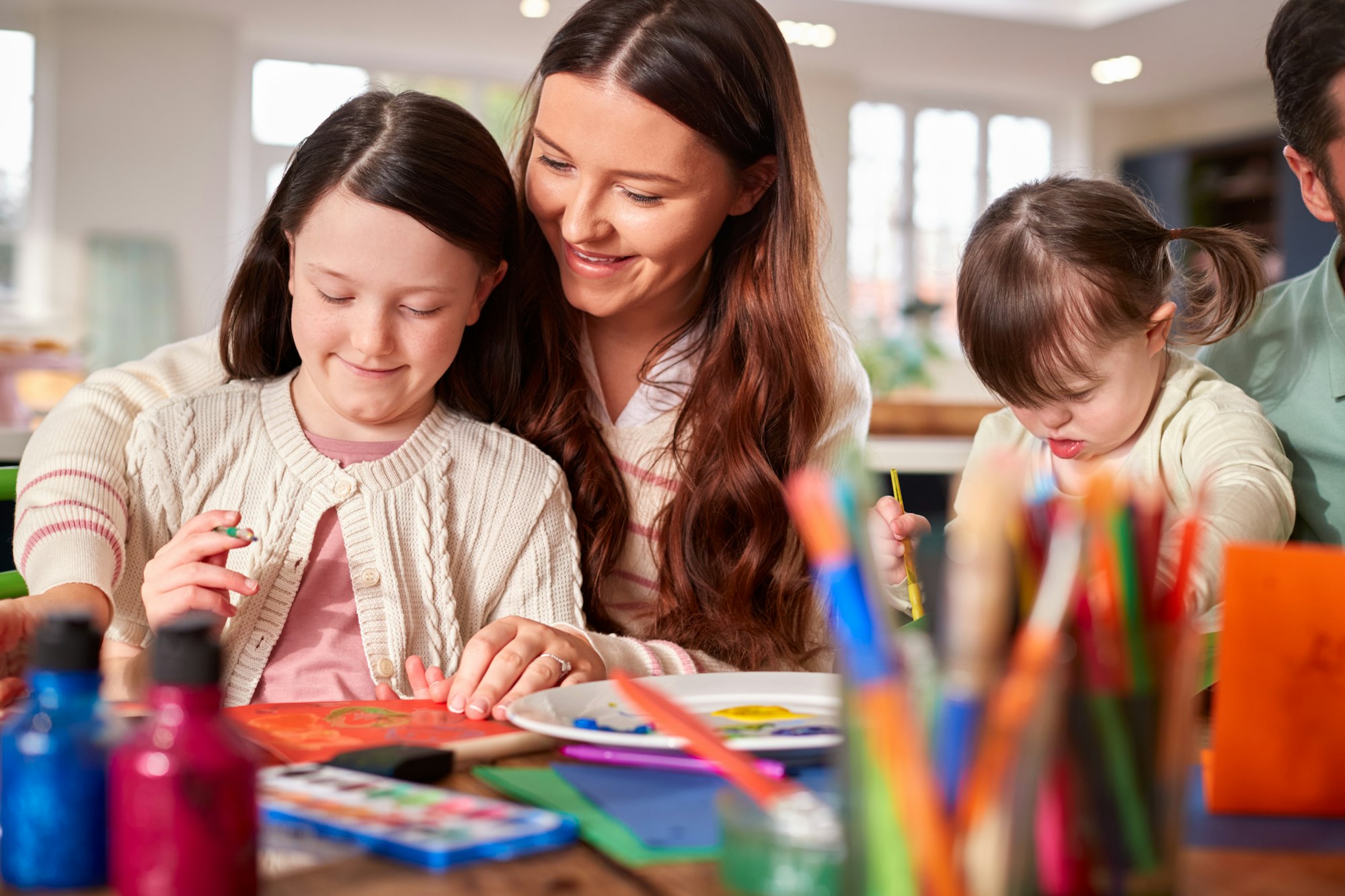 Family With Down Syndrome Daughter Sitting Around Table At Home Doing Craft Together