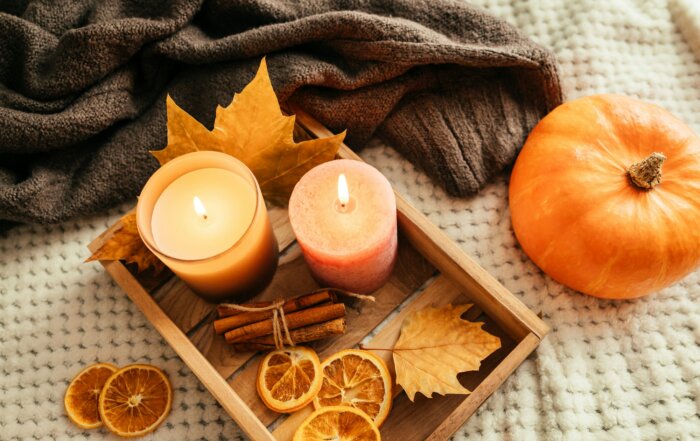 composition of a knitted sweater and autumn home decor. Candles, fallen leaves, pumpkin and cinnamon