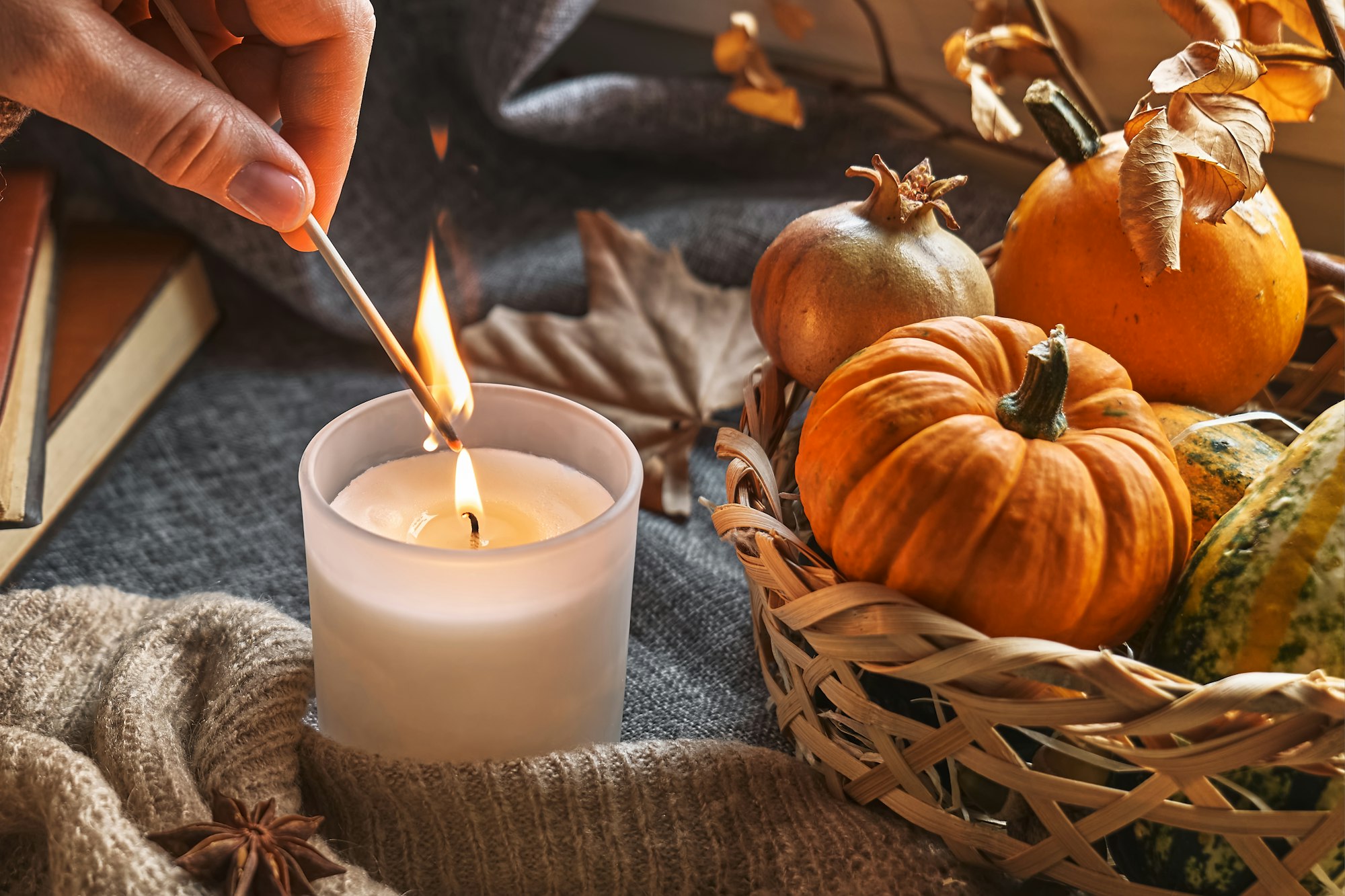 Hand with burning match lighting a candle on windowsill with cozy autumn still life with pumpkins.