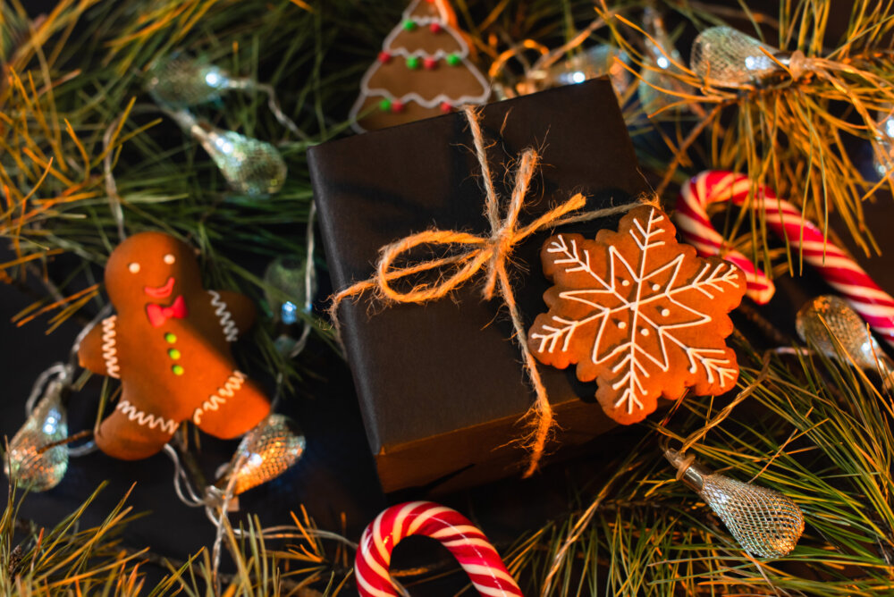 high angle view of wrapped black gift box with gingerbread cookies near green branches with garland