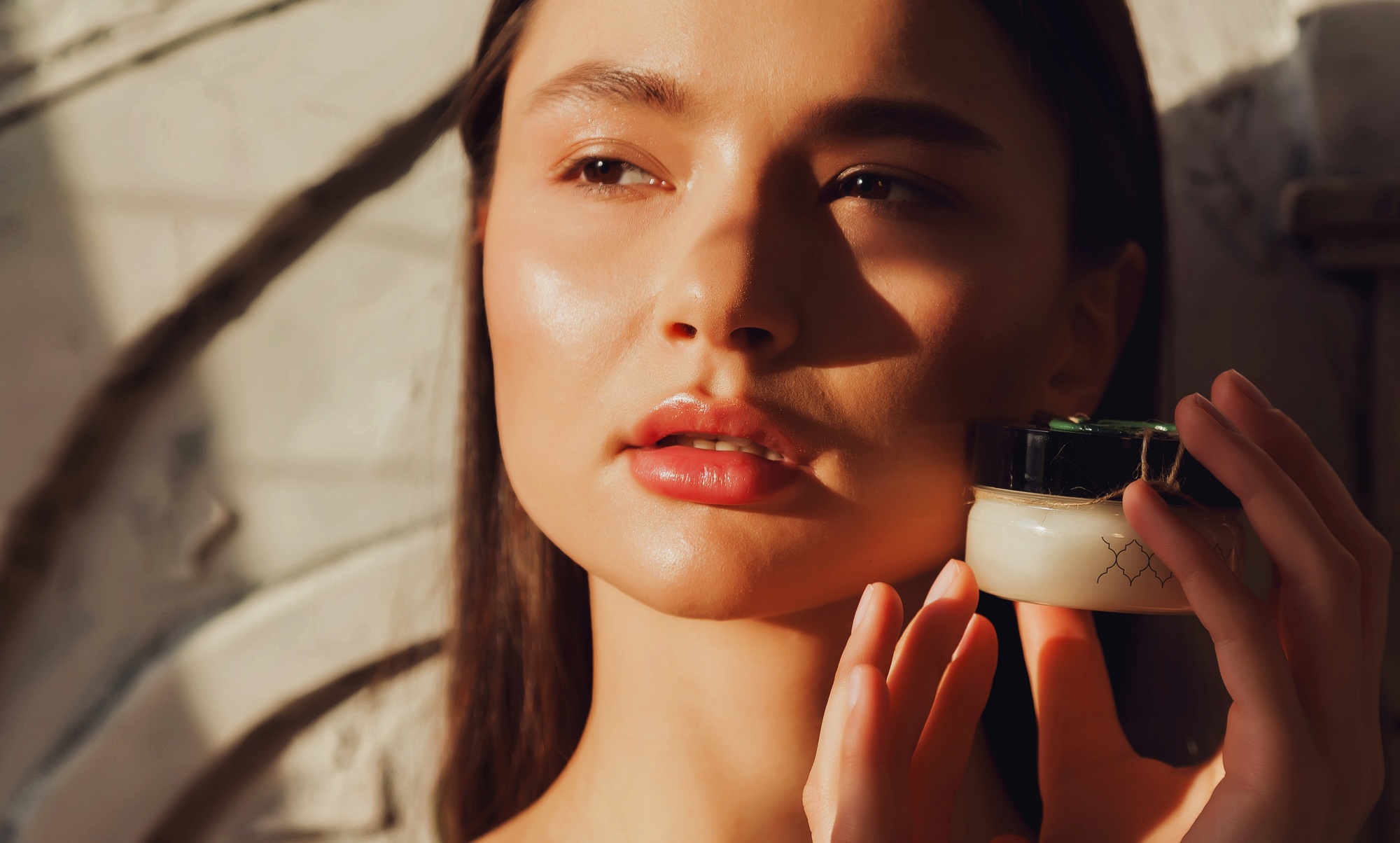 Pretty woman holding massage cream bottle near face skin in sunshine shadow